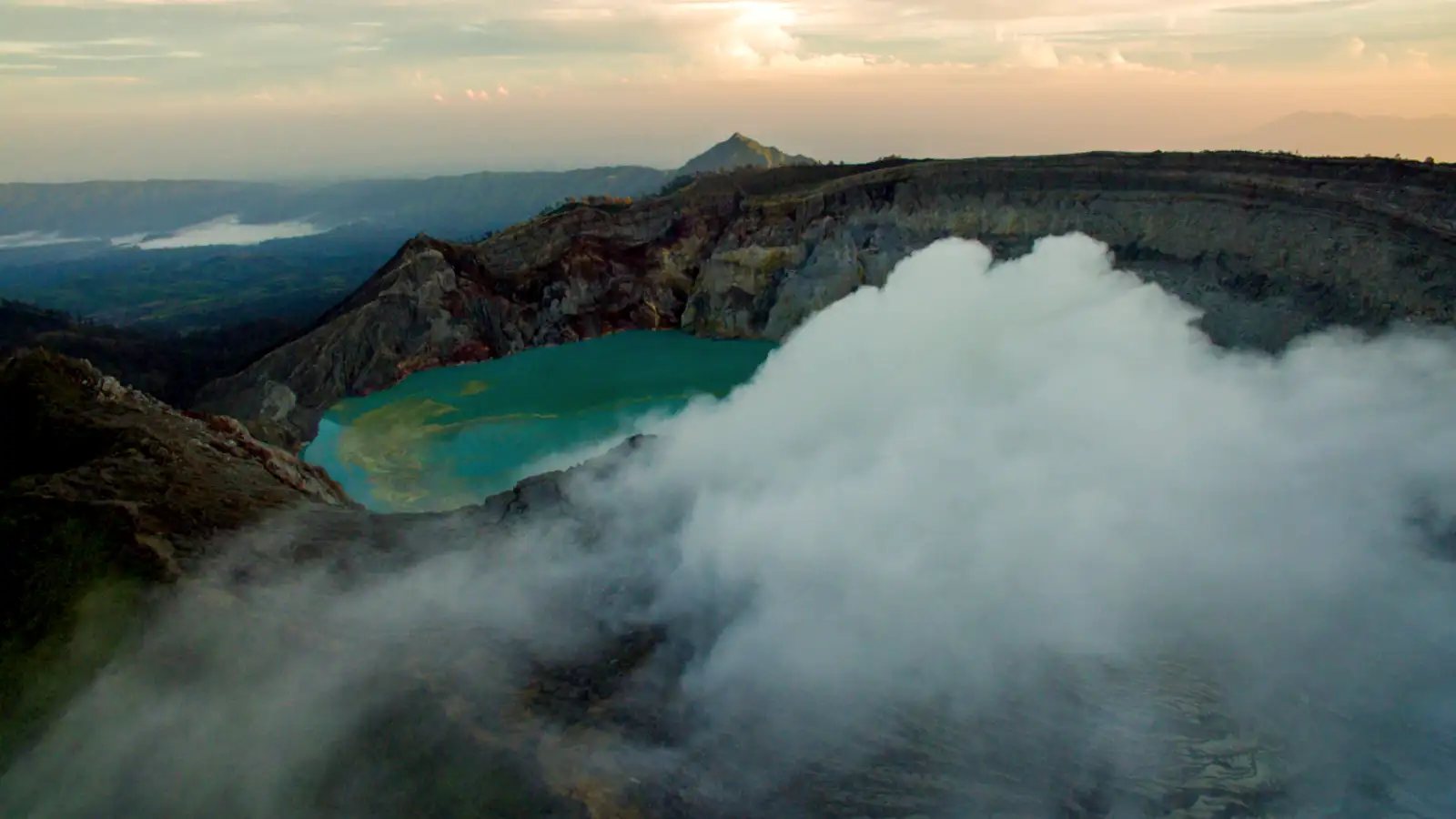Traditional sulfur miners carrying heavy baskets against the backdrop of Ijen's volcanic steam